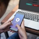 While working on laptop businessman installing OTA firmware update his smartphone at outdoor cafe