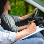 Cropped of male instructor examinating female student, taking notes at test chart while sitting by young woman driving automobile, side view, copy space, closeup.