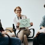Professional holding a placard with drawn smiley face while discussing Workplace Mental Health.