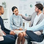 Diverse colleagues support and comfort unhappy, sad, emotional well-being coworker at team meeting or gathering. Compassionate, caring employees showing empathy to distressed woman