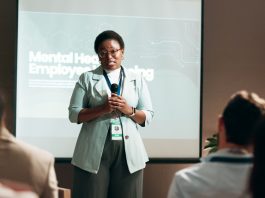 Seminar, speaker and woman with mic, talking and public speaking for mental health in workplace or stage. Business, presentation and employee with speech for audience, people and podium for presenter